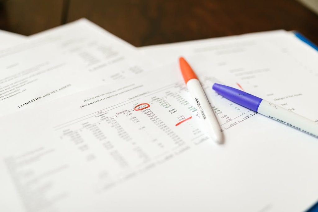 Financial documents with highlighted numbers, two markers, and accounting data on a wooden desk