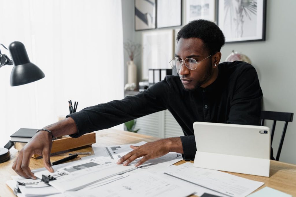 Focused man in glasses working at a desk with financial documents, a tablet, and office supplies