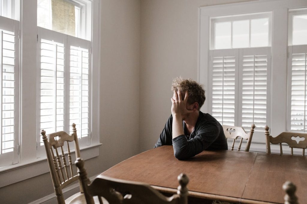 Man sitting at a wooden table with his face in his hand, looking distressed