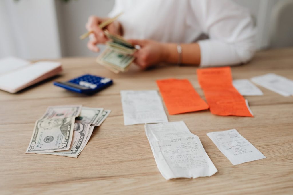 Person managing finances with cash, receipts, and a calculator on a wooden table