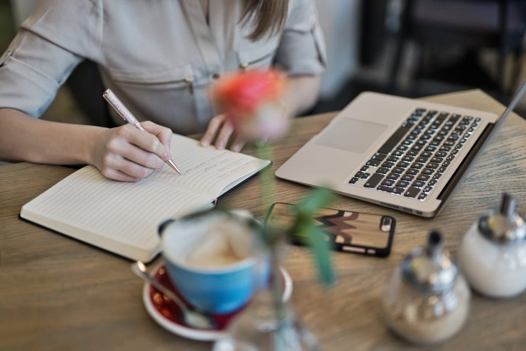 A woman writing on her notebook in front of her laptop