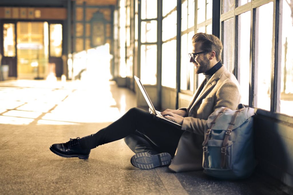 A man on his laptop outside leaning into the hallway windows