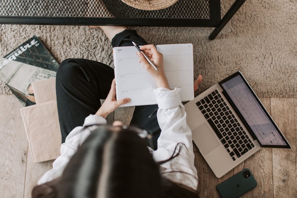 Faceless woman working on a laptop and notebook at home, developing a production guide for her micro-course