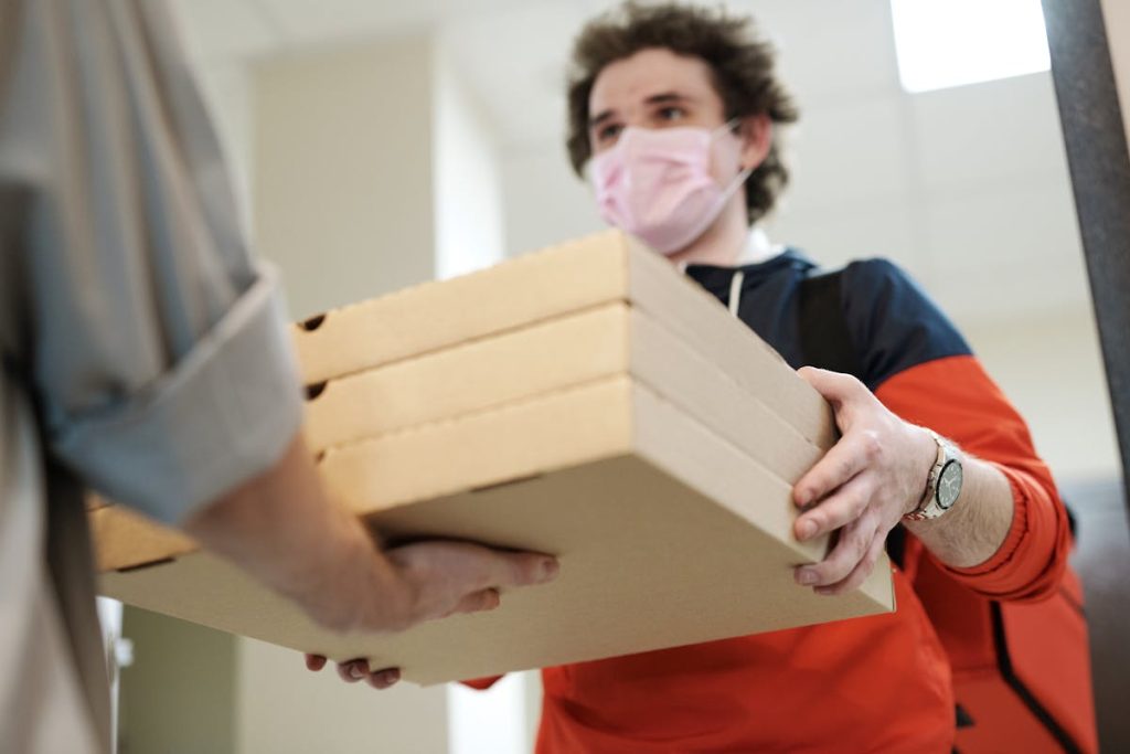 Man wearing a face mask delivering pizza, representing flexible income from food and grocery delivery