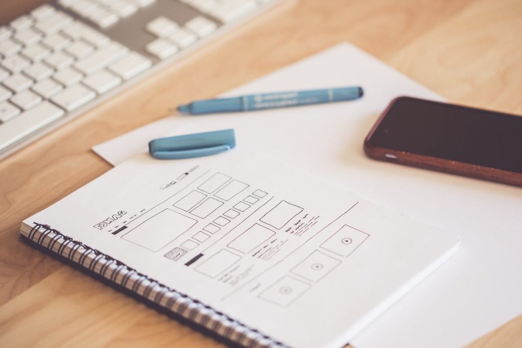 Website wireframe drawn on paper beside pen and phone, visualizing the structure of the Weekend Website Formula.