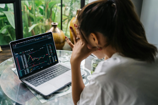 Woman looking stressed while checking stock market charts on a laptop at a glass table.