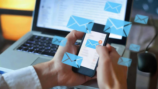 An Email Marketer Checking out his mails with his phone while sending more with his laptop
