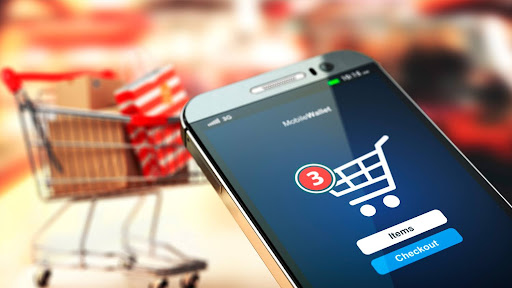 A smartphone displaying a shopping cart app, with a physical shopping cart visible in the background