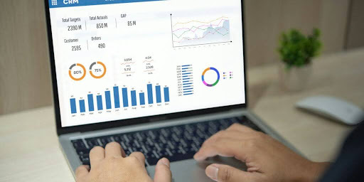 A person sitting at a desk using a laptop displaying a sales graph on the screen.