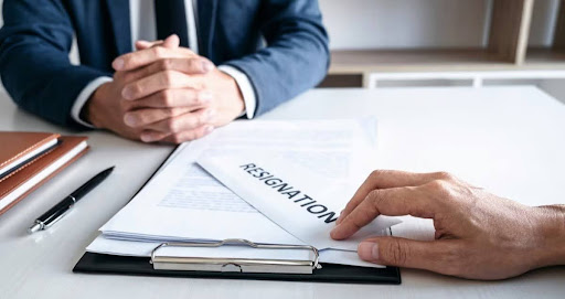 A man tenders his resignation letter on a desk while his boss observes attentively