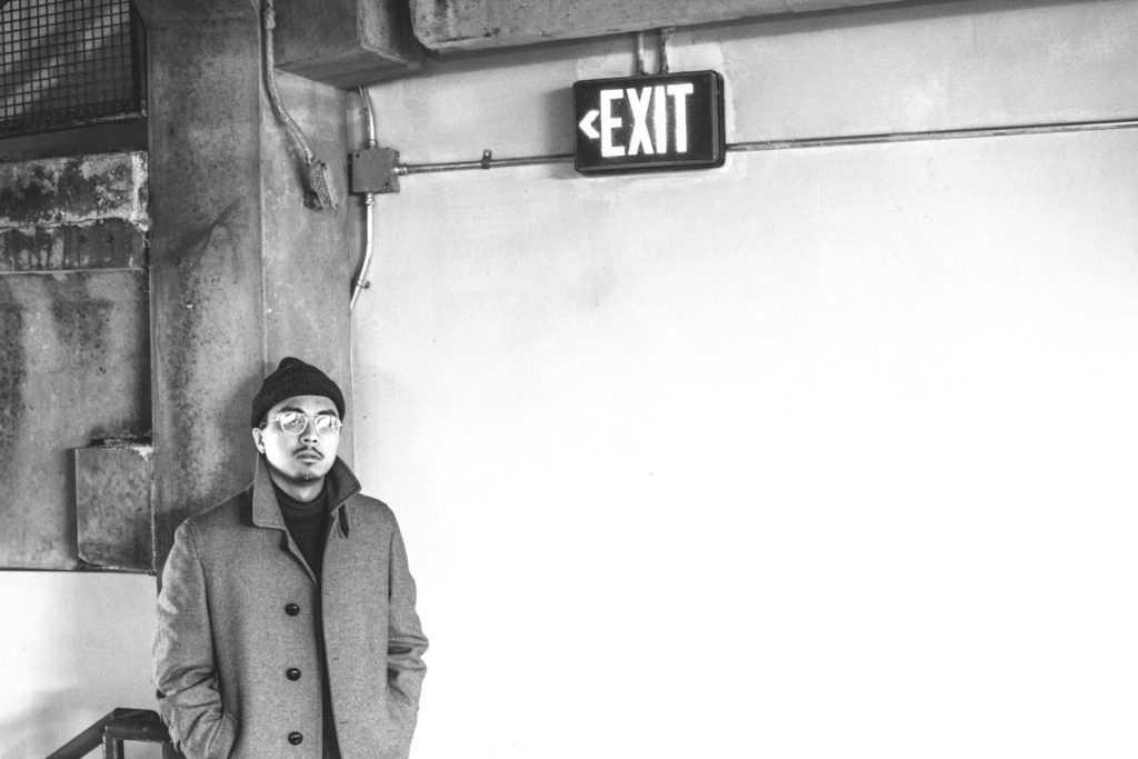 Grayscale photo of a man standing near an exit sign, symbolizing leaving a toxic job
