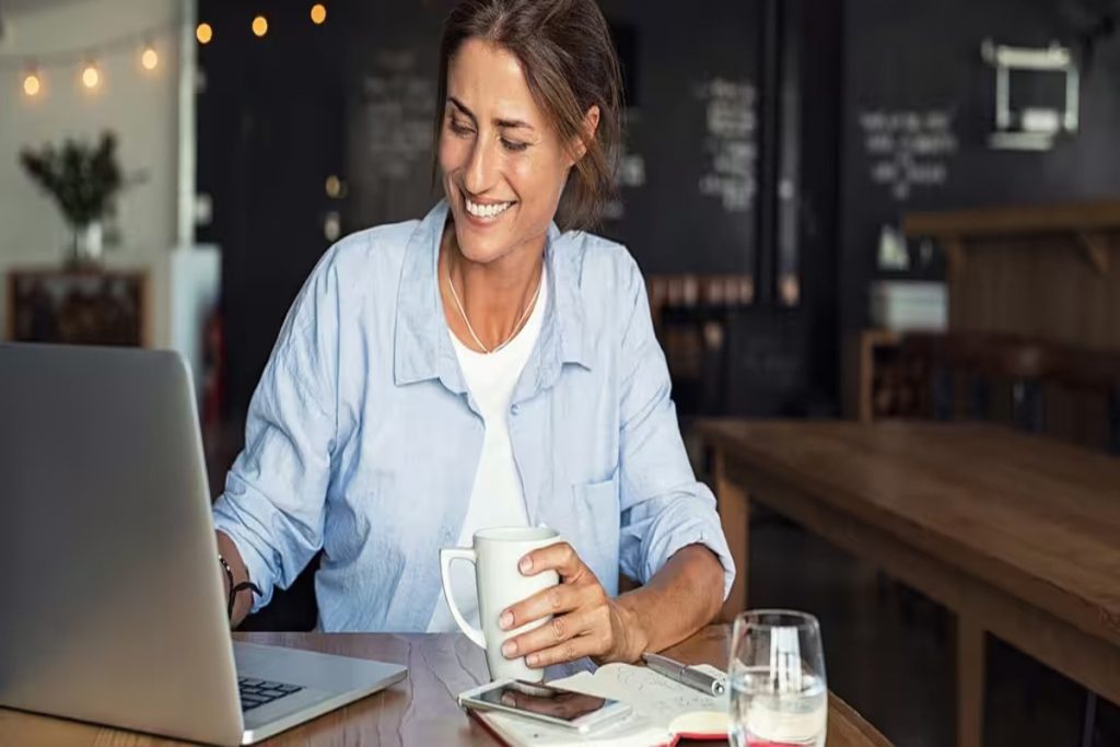 A freelancer smiling while she drinking a cup of coffee and typing