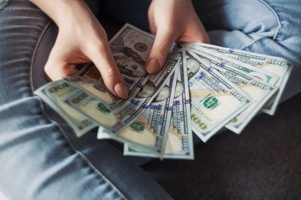 A person holding a stack of $100 dollar bills in his hands